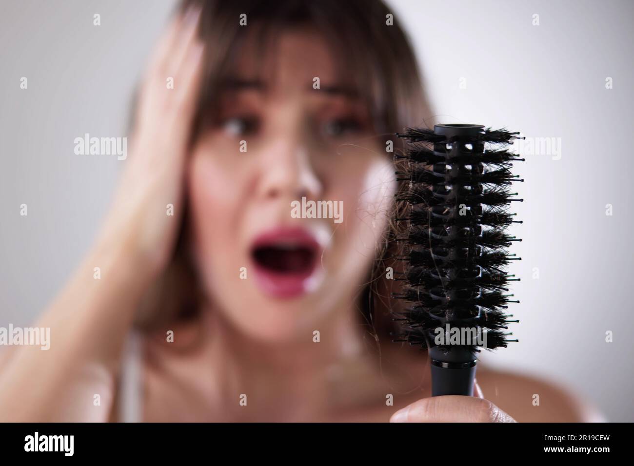 Young Woman In Bathrobe Holding Comb Looking At Hair Loss At Home Stock Photo