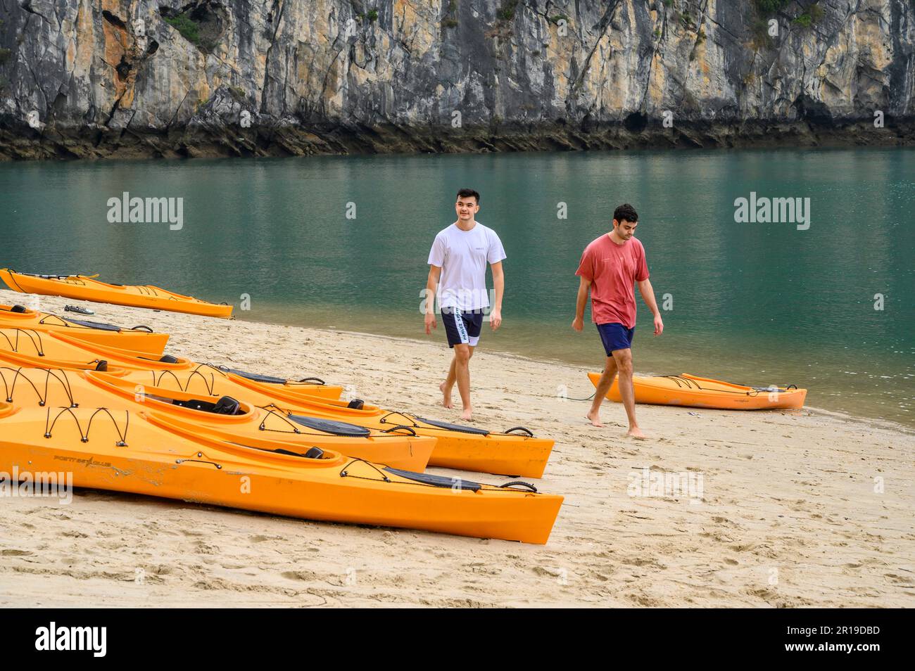 Two young men walking on a beach with kayaks ready to launch in Bai Tu