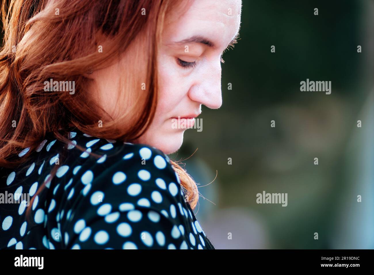 Portrait of a beautiful woman with red hair, contemplating and thinking about , looking sad, gazing down. With a broken spirit expression. Stock Photo