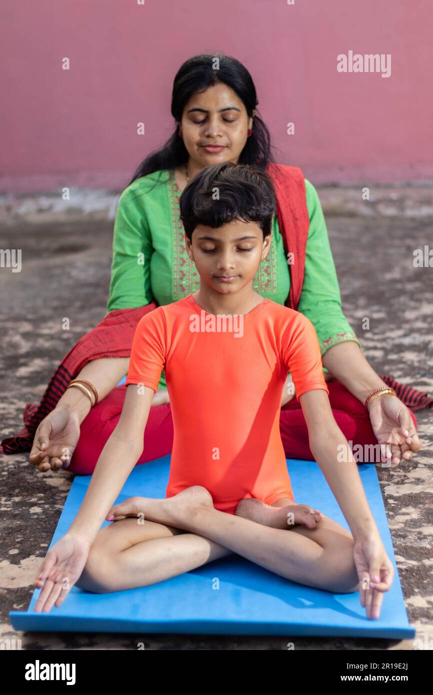 An Indian girl child with mother practicing padmasana yoga on yoga mat ...