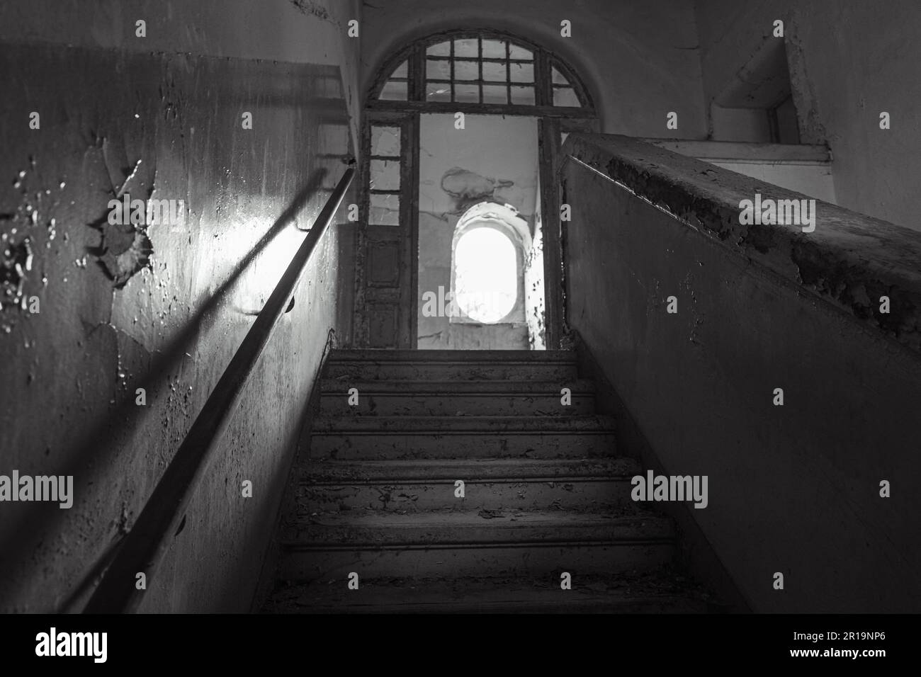 An aged building with a shadowy set of steps leading up to the entrance, greyscale Stock Photo