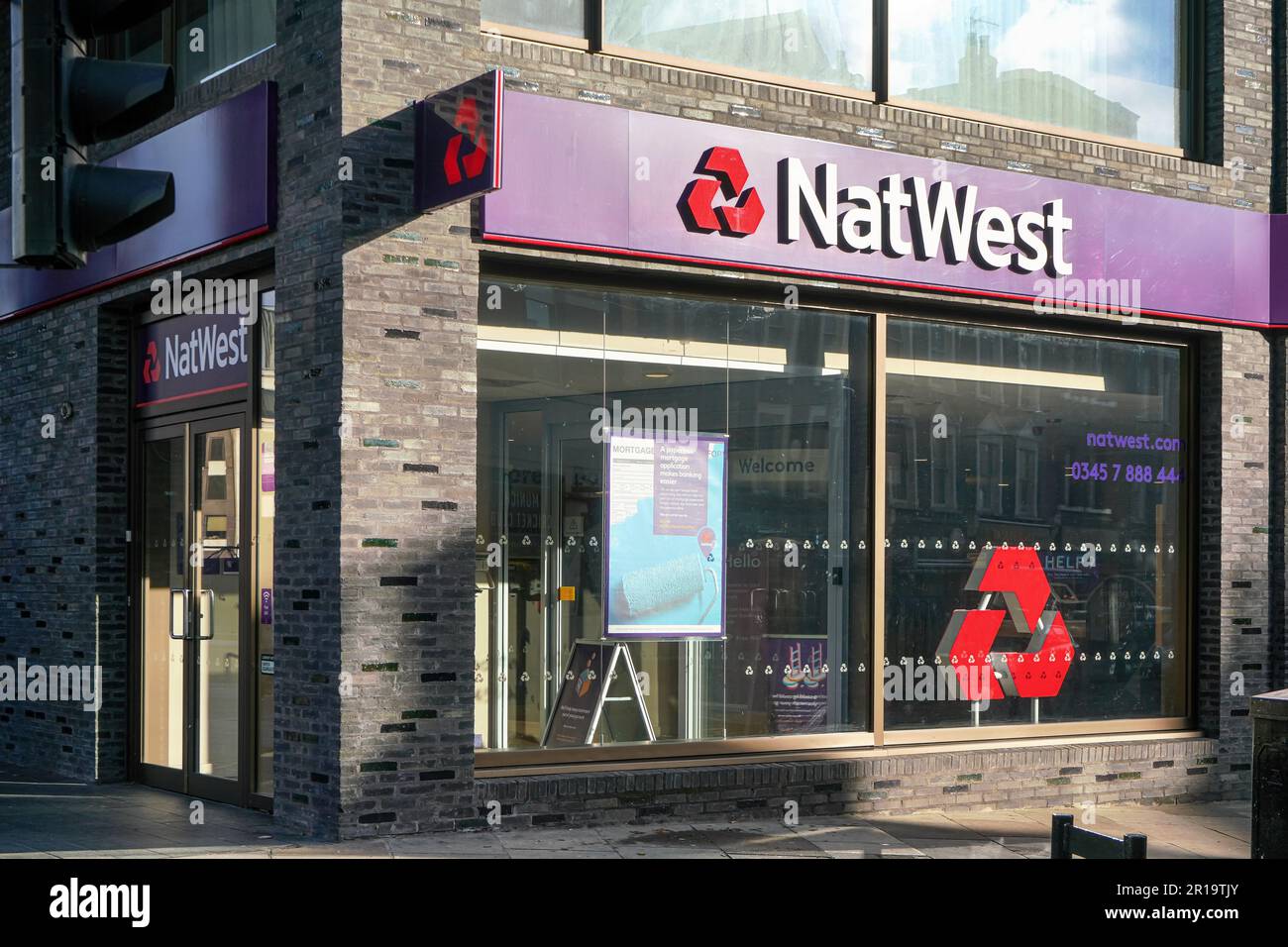 London, United Kingdom - February 02, 2019: Sun shines on stone bricks wall at one of National Westminster Bank branches, with red purple logo. It is Stock Photo