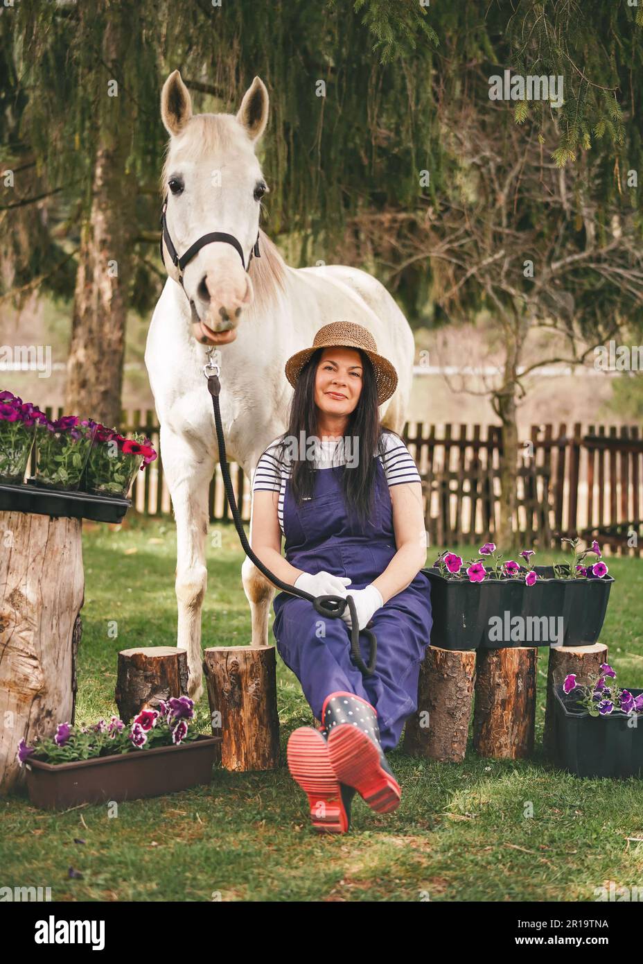 Woman in work clothes, gloves, rubber boots and straw hat sitting near