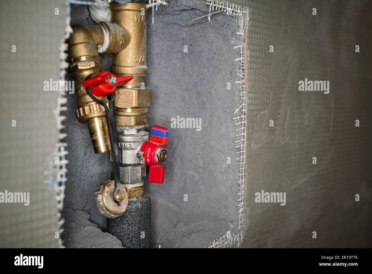 Newly installed brass water pipes plumbing with red tap fittings, gray cement wall reinforced