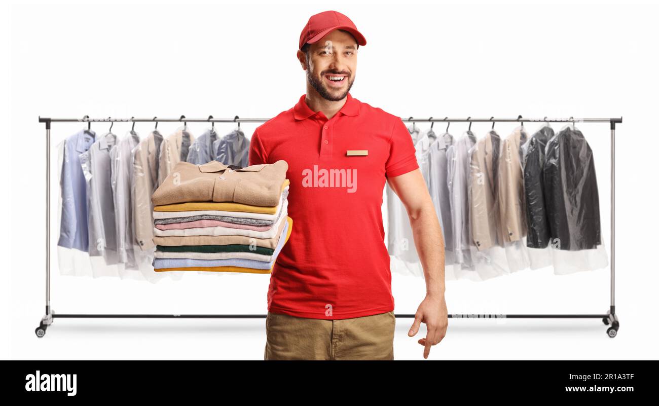 Male worker holding a pile of folded clothes in front of clothing racks at dry cleaners isolated on a white background Stock Photo