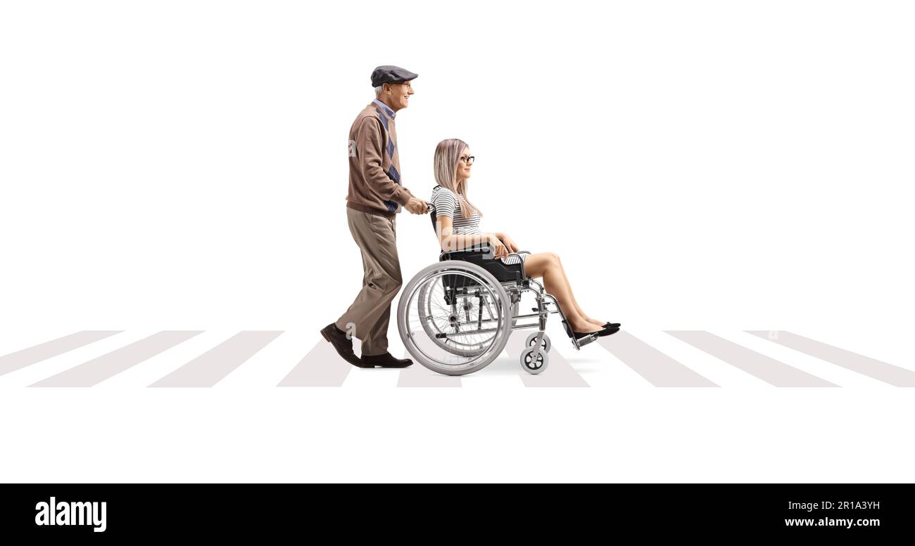 Full length profile shot of an elderly man pushing a young woman in a wheelchair at a pedestrian crossing isolated on white background Stock Photo