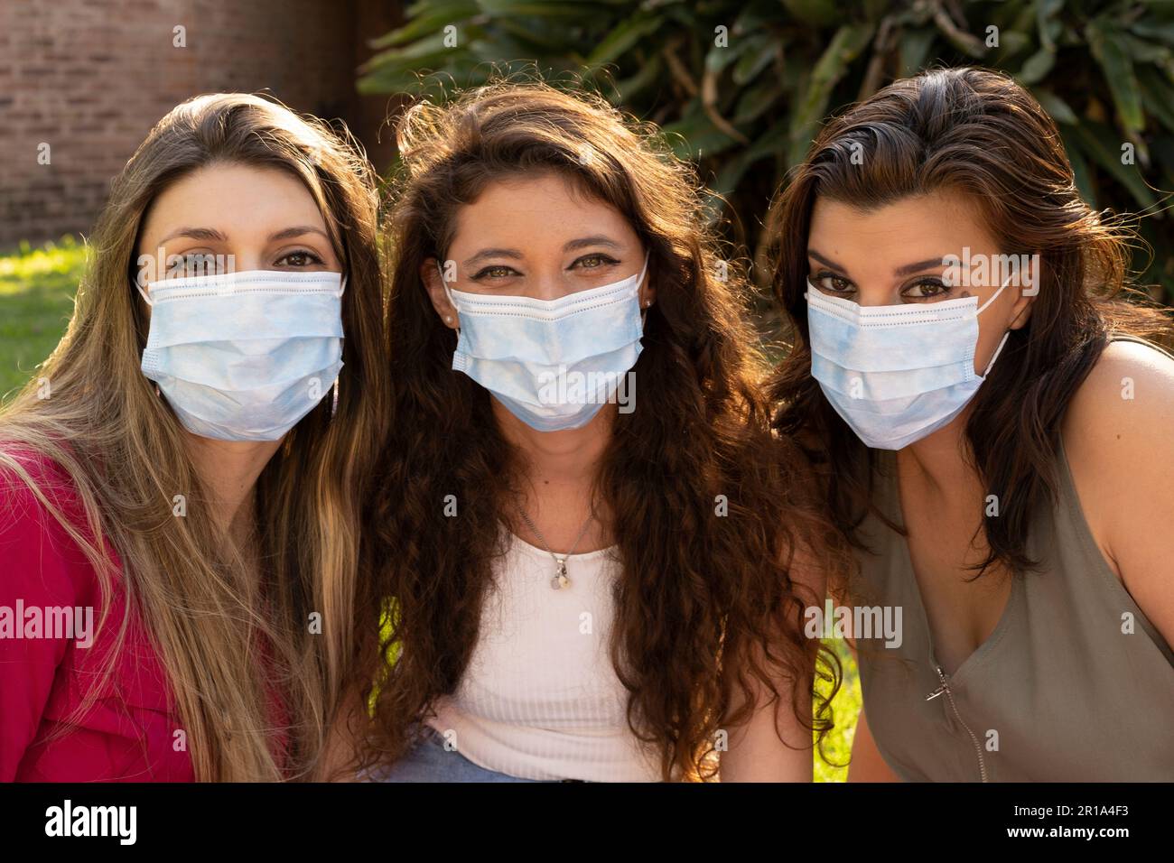 Three smiling girl friends wearing masks looking at camera Stock Photo