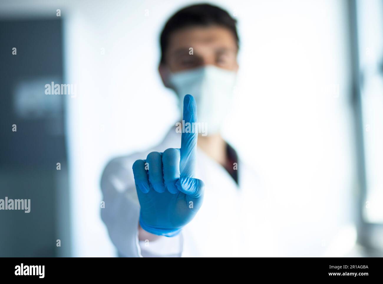 A medical doctor in protective gloves holding up an index finger while standing in a hospital setting Stock Photo