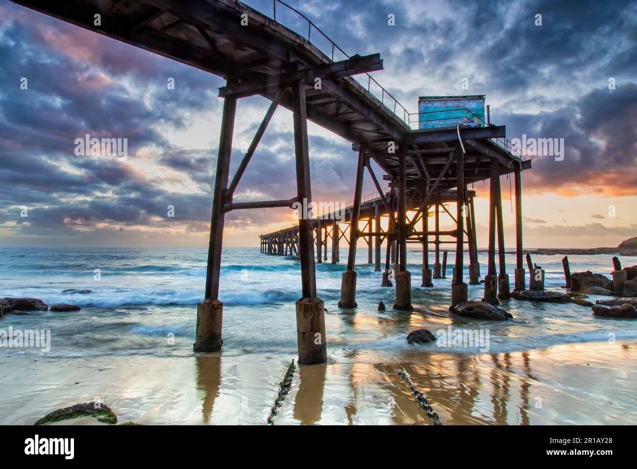 Under long historic timber jetty at Middle camp beach in Catherine Hill bay coastal town of Australia at sunrise. Stock Photo