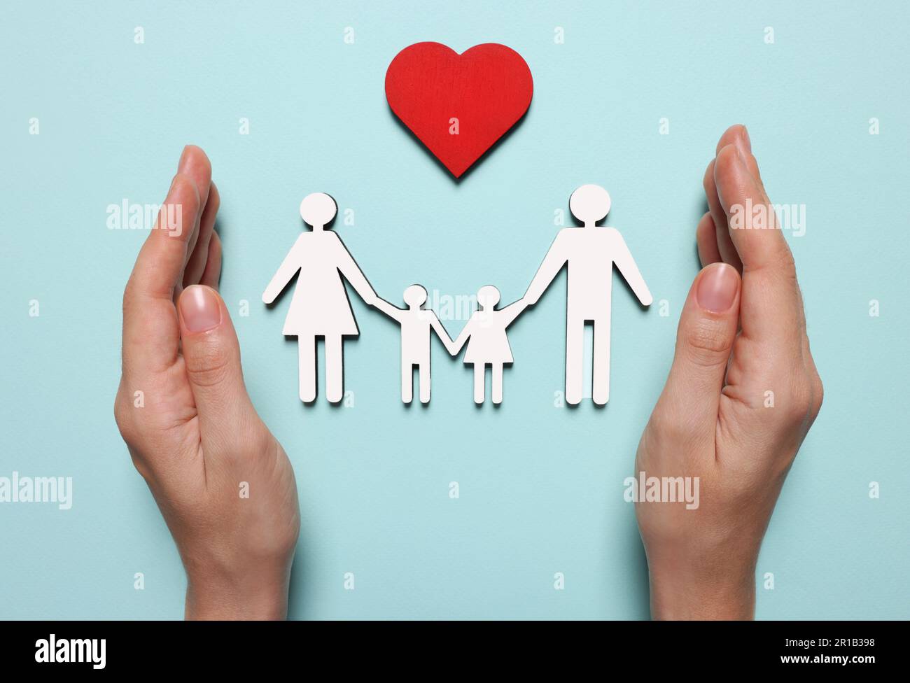 Woman protecting figures of family and heart on light blue background, top view. Insurance concept Stock Photo