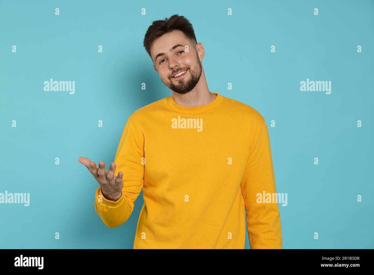 Handsome man in yellow sweatshirt gesturing on light blue background Stock Photo