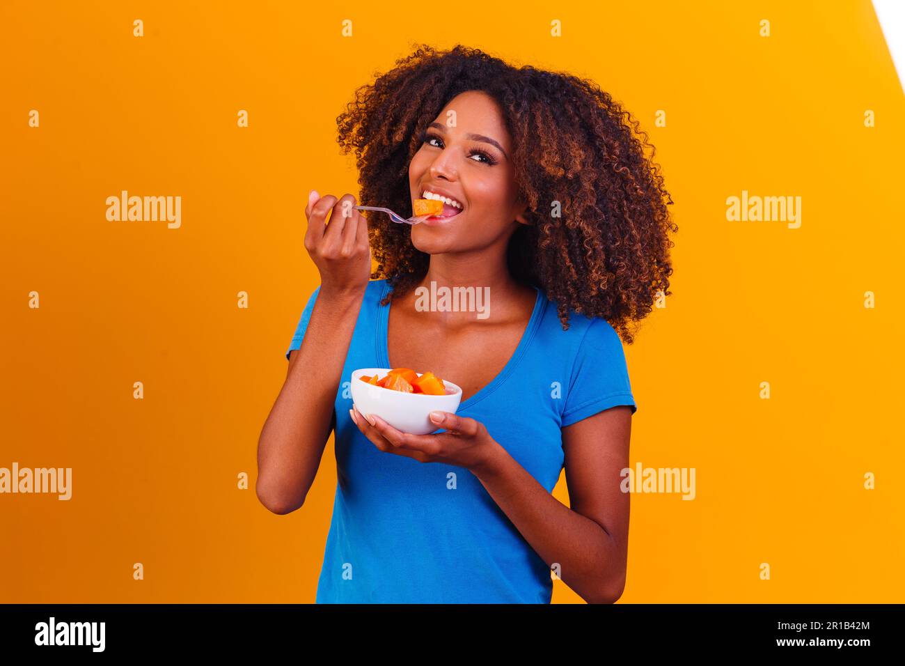 afro girl eating papaya from the bowl. Healthy eating concept Stock