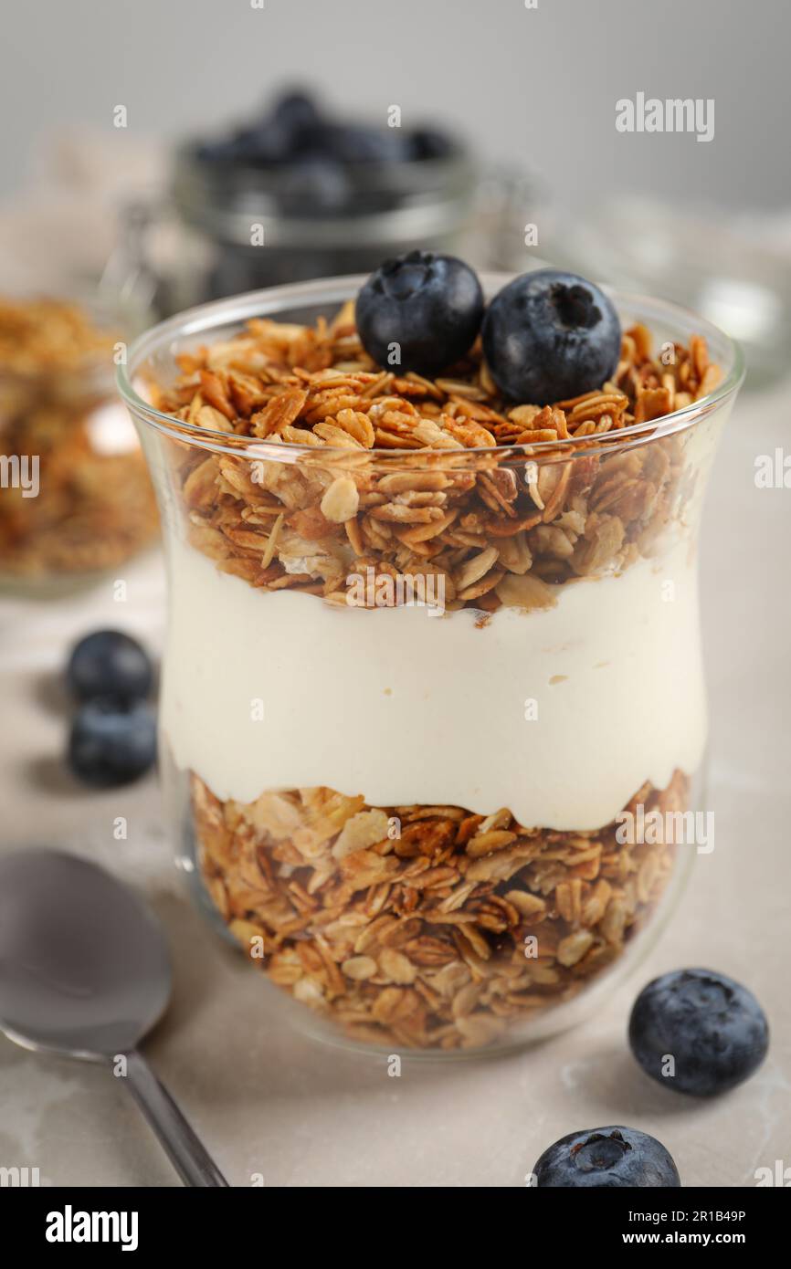 Glass of yogurt with granola and blueberries on grey marble table, closeup Stock Photo