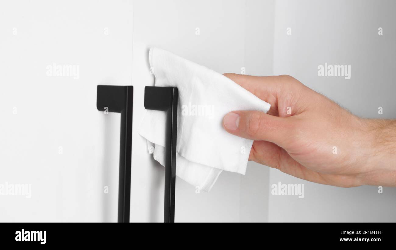 Man cleaning wardrobe handle with disinfecting wipe indoors, closeup. Protective measures Stock Photo