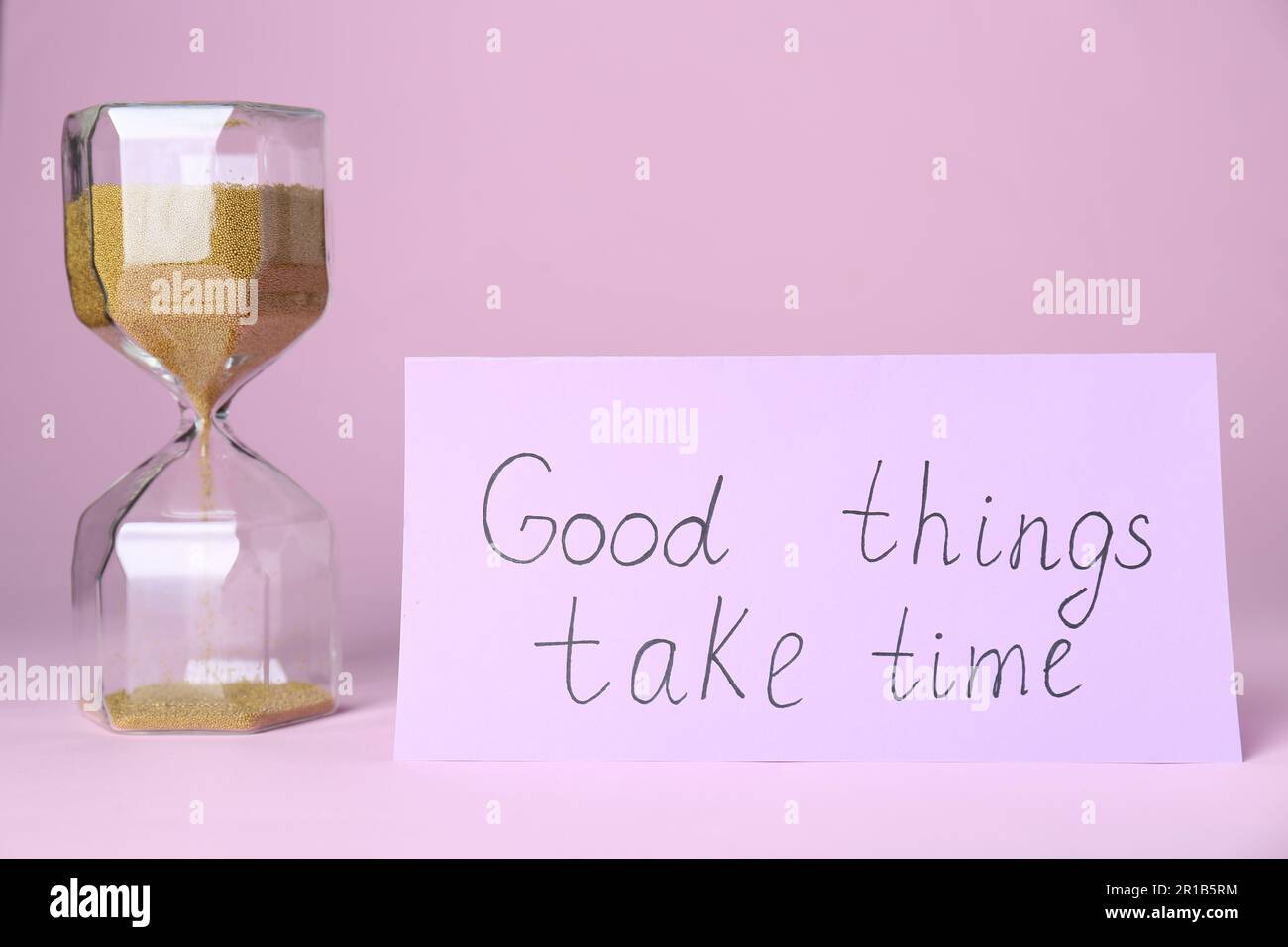 Card with phrase Good Things Take Time and sand clock on pink ...