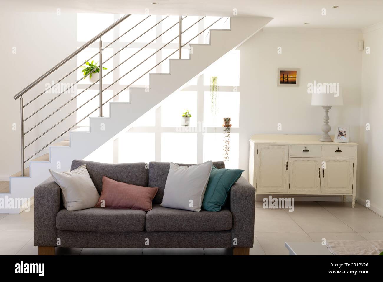 Sofa with cushions arranged against staircase and electric lamp on cabinet in living room at home Stock Photo