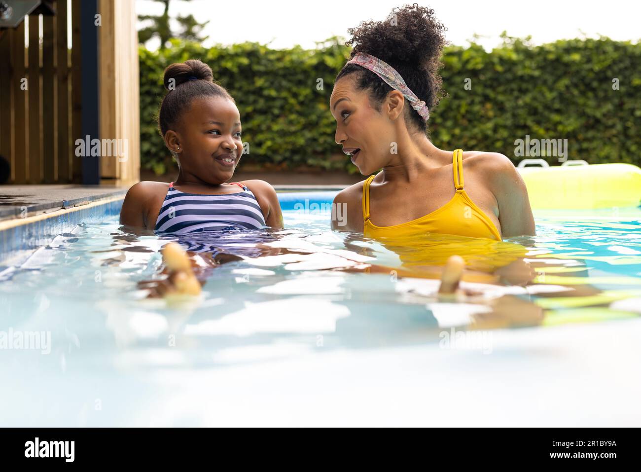 Happy african american mother and daughter talking lying in swimming