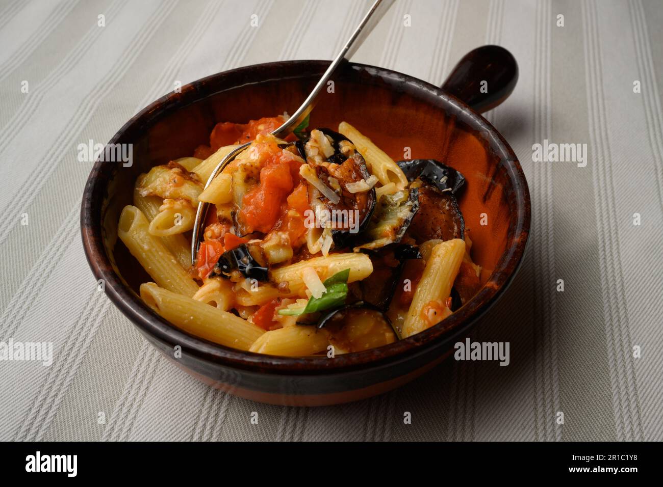 Pasta alla Norma or Penne Rigate with Eggplant and Tomato Sauce and Ricotta in a Rustic Terracotta Bowl Stock Photo