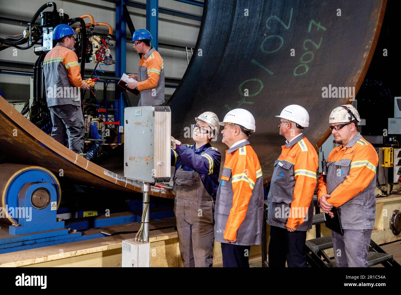 Nordenham, Germany. 12th May, 2023. Janina Patricia Schweitzer (l-r), a production employee at Steelwind Nordenham GmbH, shows German Chancellor Olaf Scholz (SPD), Andreas Liessem, managing director of Steelwind Nordenham GmbH, and Jörg Redmer, a production employee, the function of the longitudinal internal seam welding machine used to manufacture steel foundations for wind turbines. Scholz visited the production of steel foundations, so-called monopiles, for wind turbines in offshore wind farms at Steelwind Nordenham GmbH. Credit: Hauke-Christian Dittrich/dpa/Alamy Live News Stock Photo