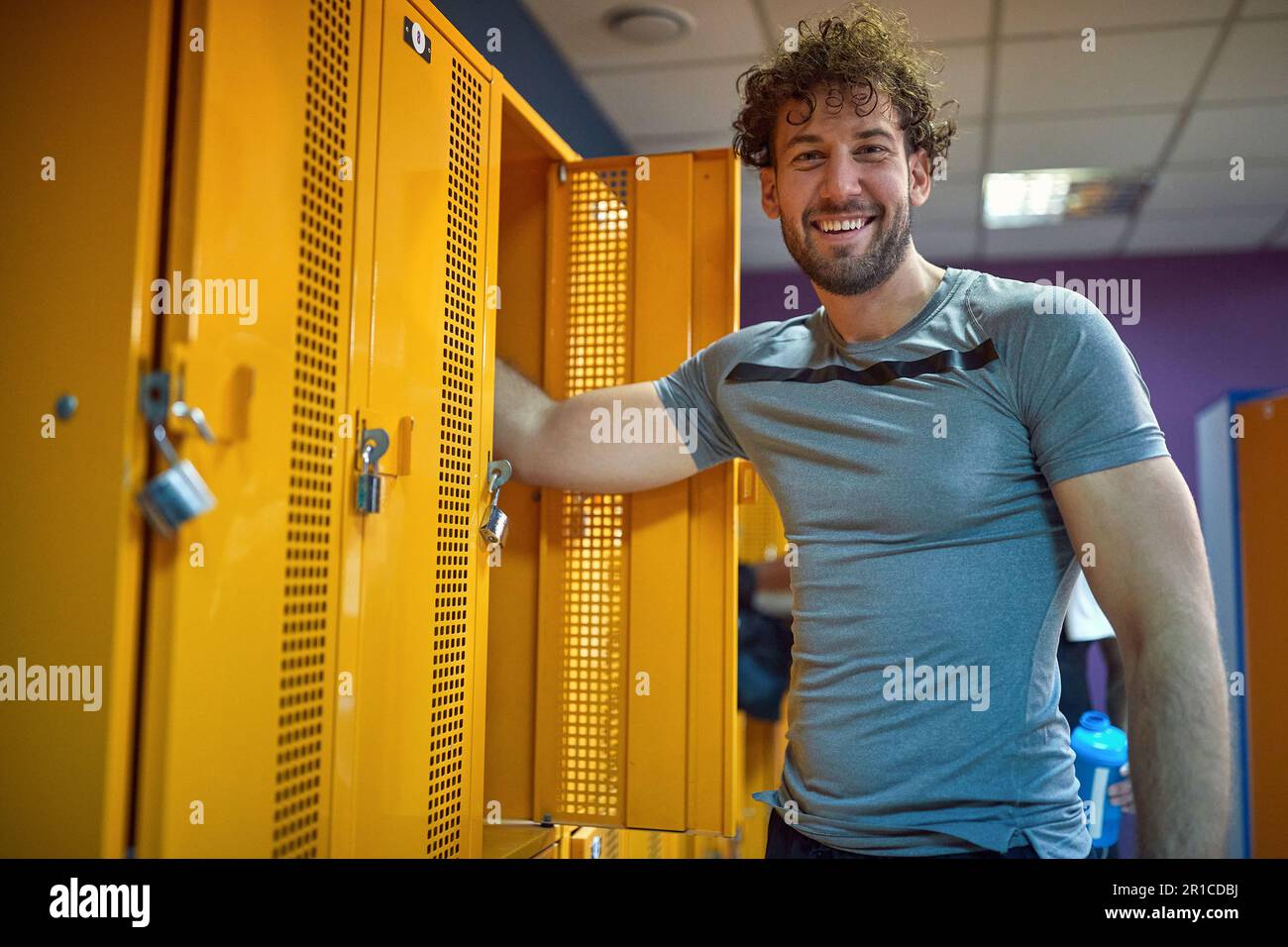 Cheerful young man standing in gym locker room, getting ready for workout session. Health, lifestyle concept. Stock Photo