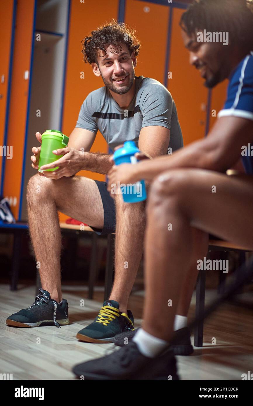 Young men in the locker room after workout, sitting on bench, resting. Sports, health, lifestyle concept. Stock Photo
