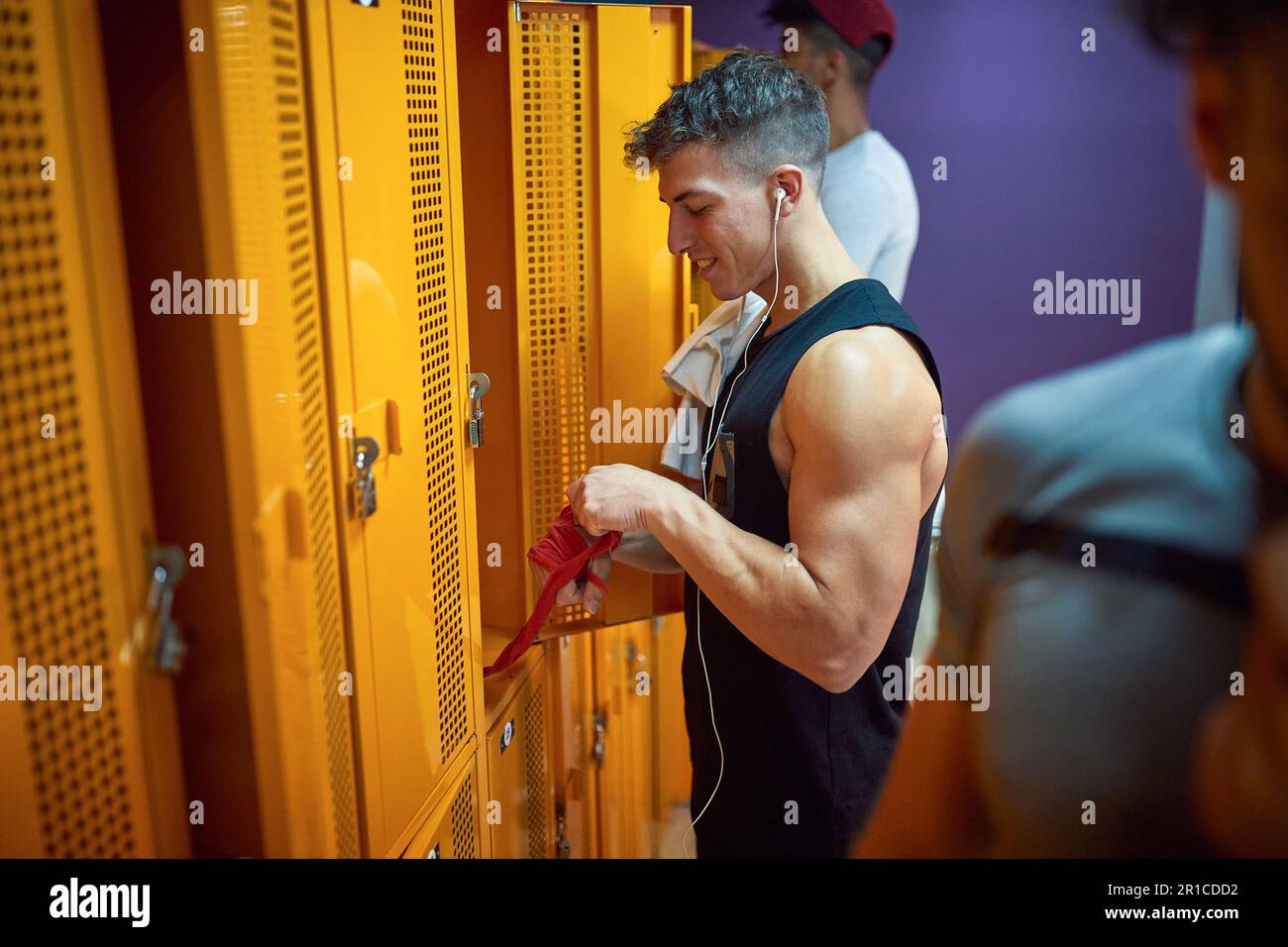 Young man taking red protective tape off his hand in the gym locker room, after workout. Sports, health, lifestyle concept. Stock Photo