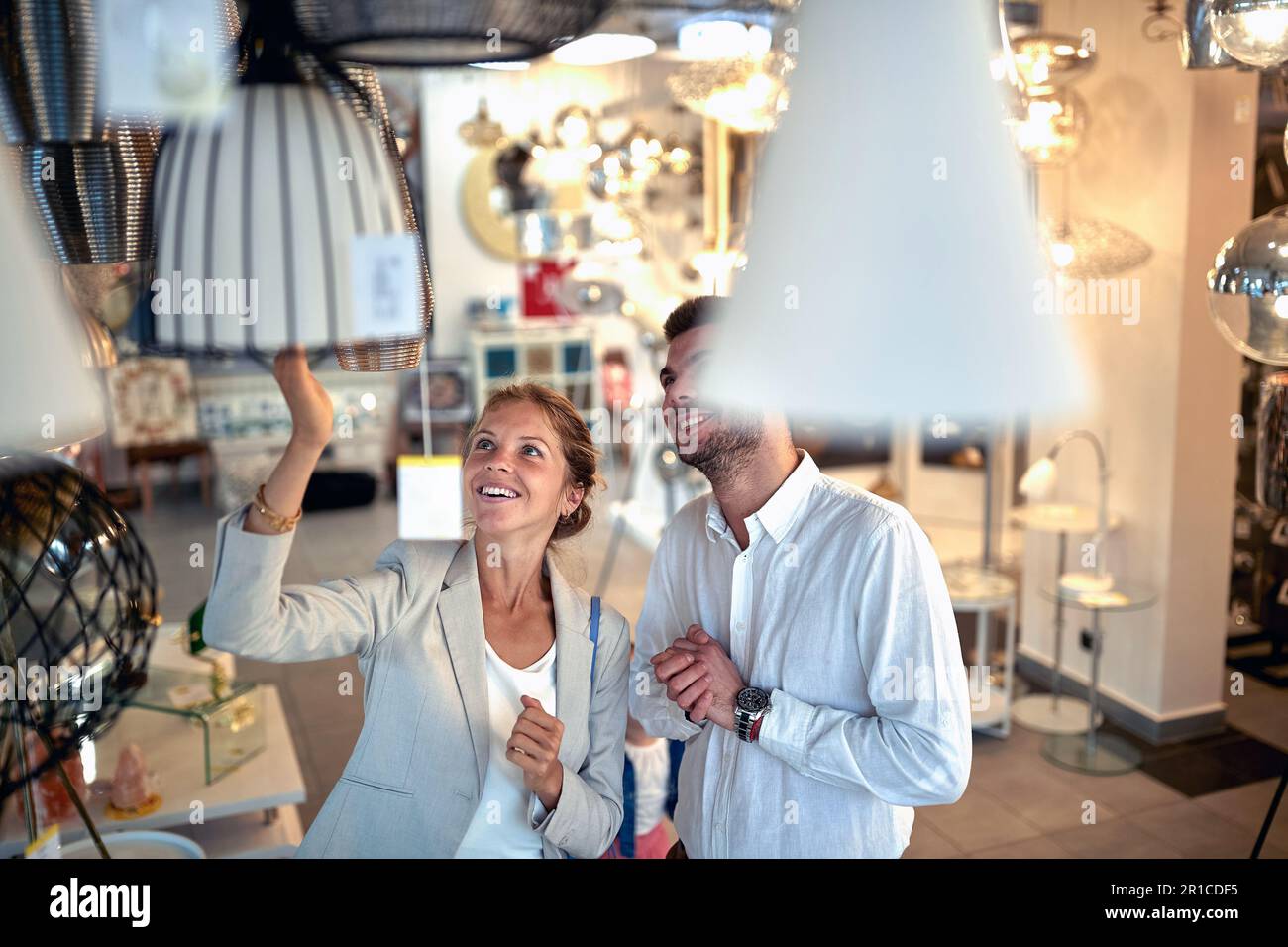 Young couple in a lighting store, browsing through chandeliers and lamps with excitement and joy on their faces. Stock Photo