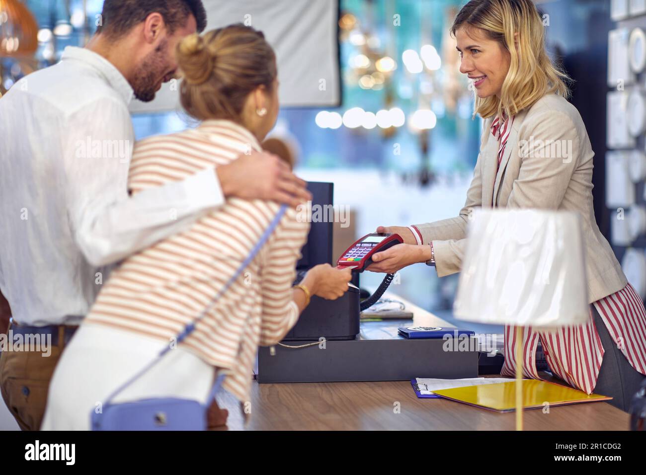 Smiling cashier processing credit card payment for young couple's purchase at lighting store Stock Photo