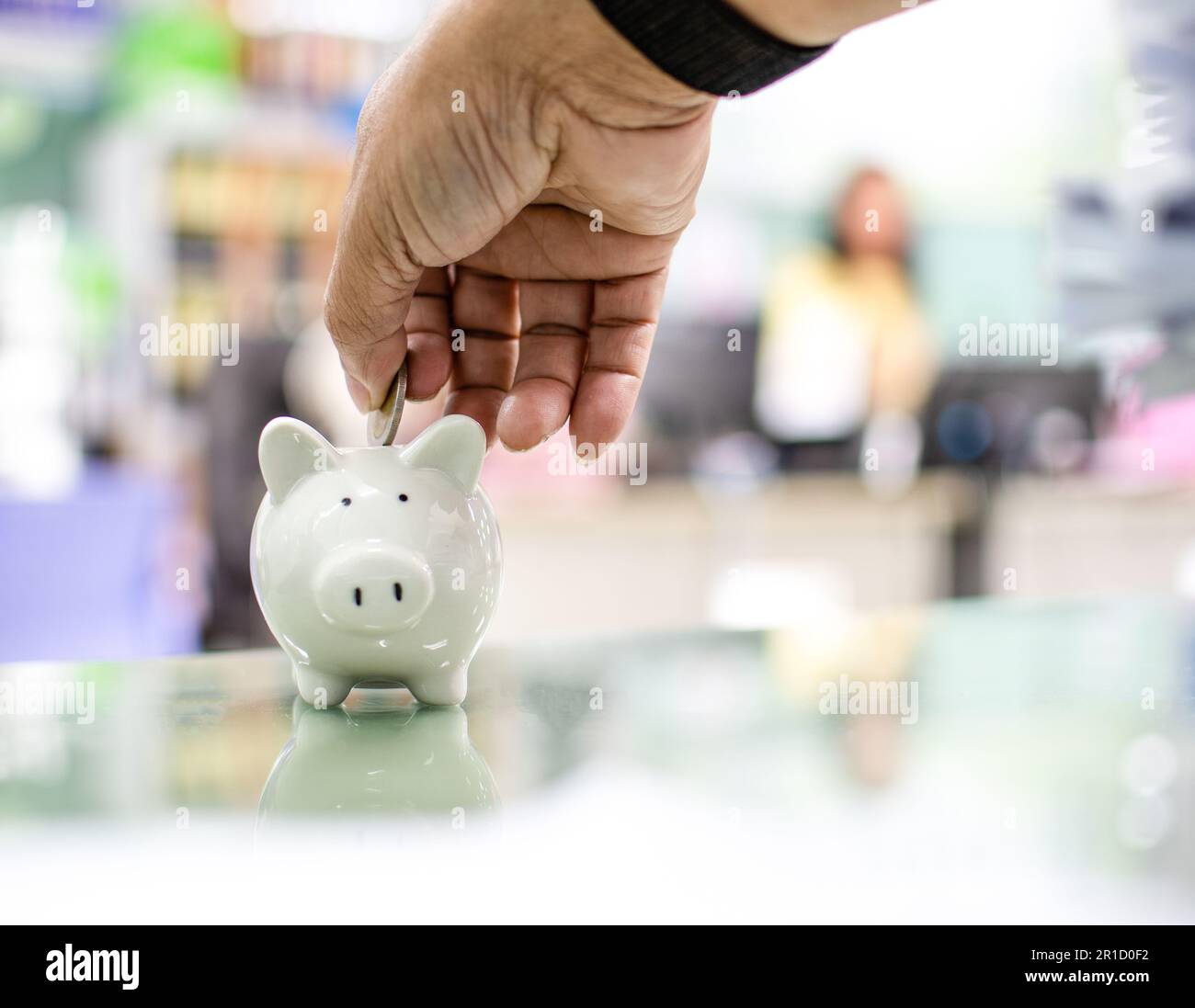 Close up. Hand of a man holding a coin for putting to white piggy bank ...