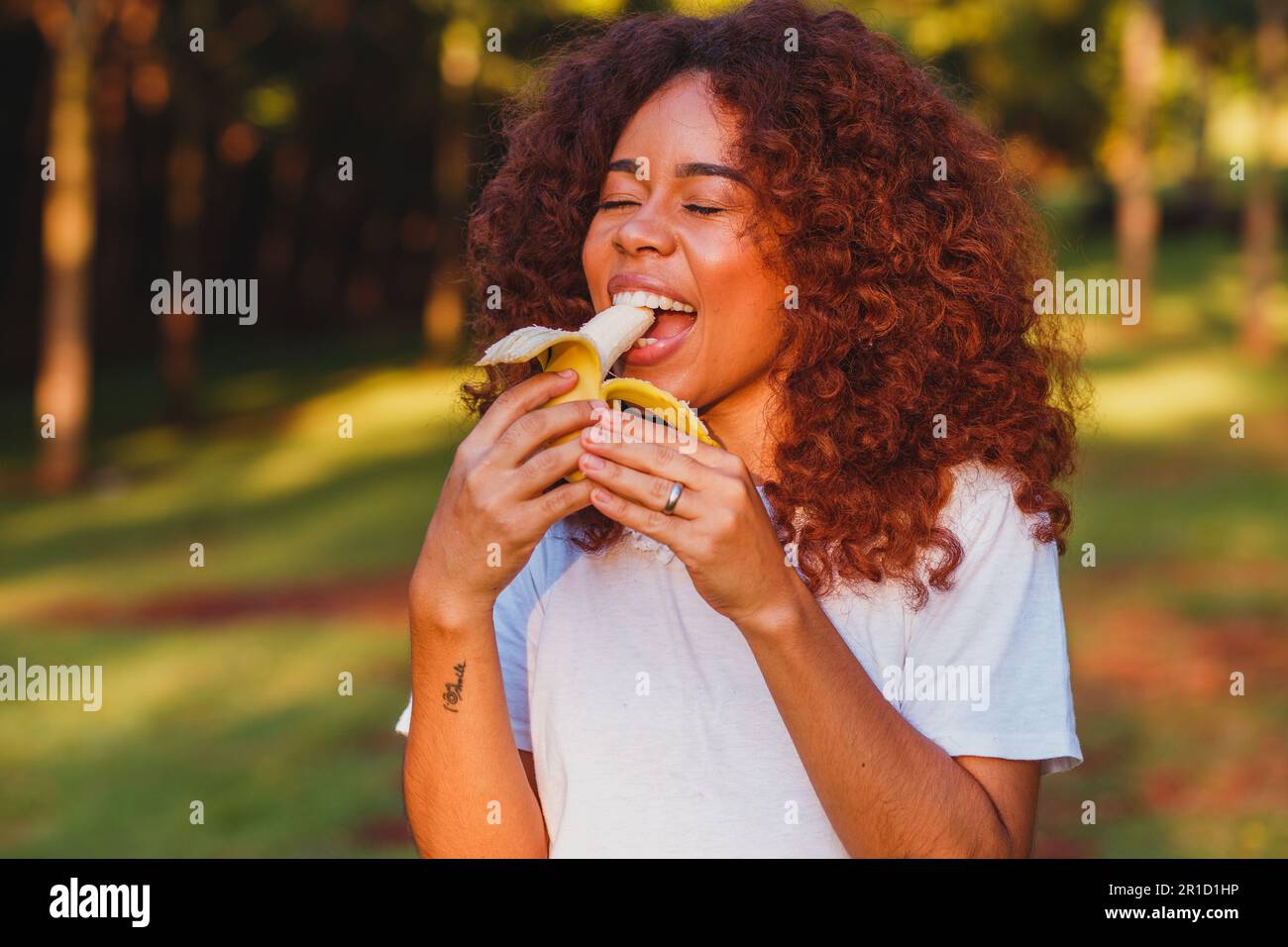 Afro woman eating banana in the park. Healthy living concept Stock