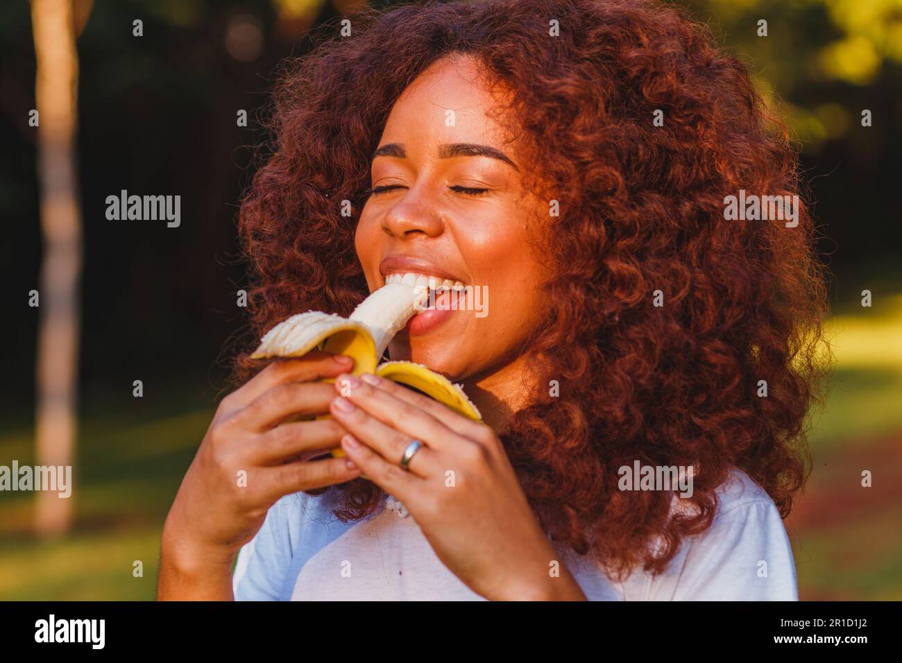 Afro woman eating banana in the park. Healthy living concept Stock