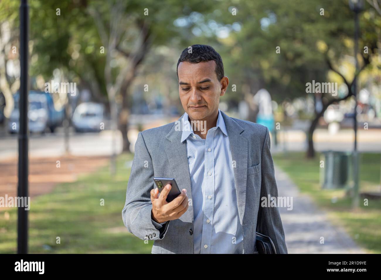 Young latin man in suit walking with mobile phone in hand with copy space. Stock Photo