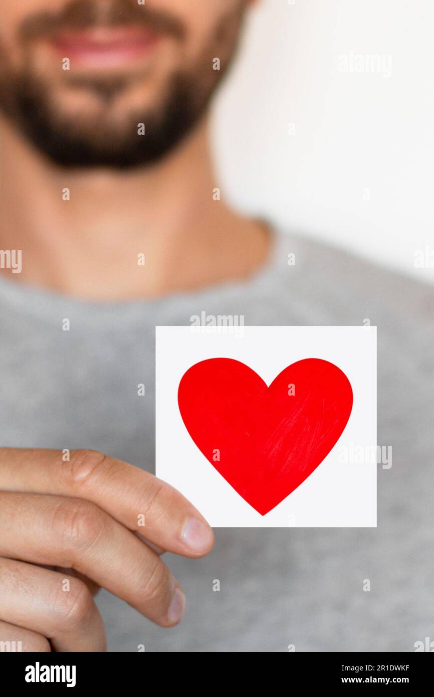 A close-up of a man holding a piece of paper with a red heart on it Stock Photo