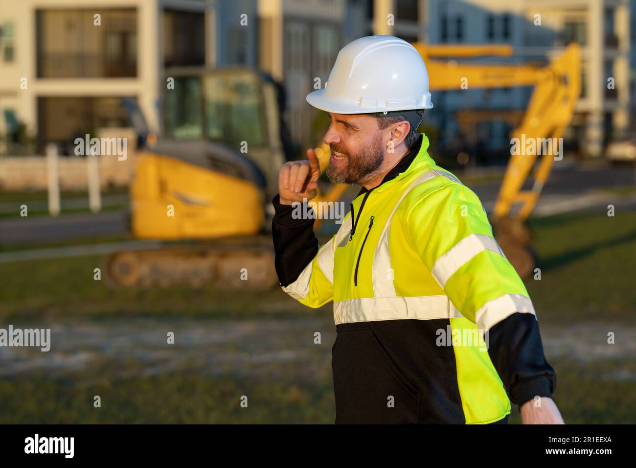 Caucasian man, construction worker in helmet at construction site. Industry engineer worker in hardhat near bulldozer or digger tractor. Concept of co Stock Photo