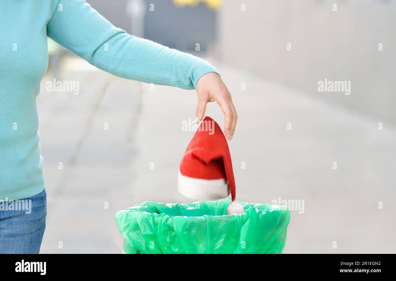 Woman throwing a santa hat to the trash in a trash bin a city after