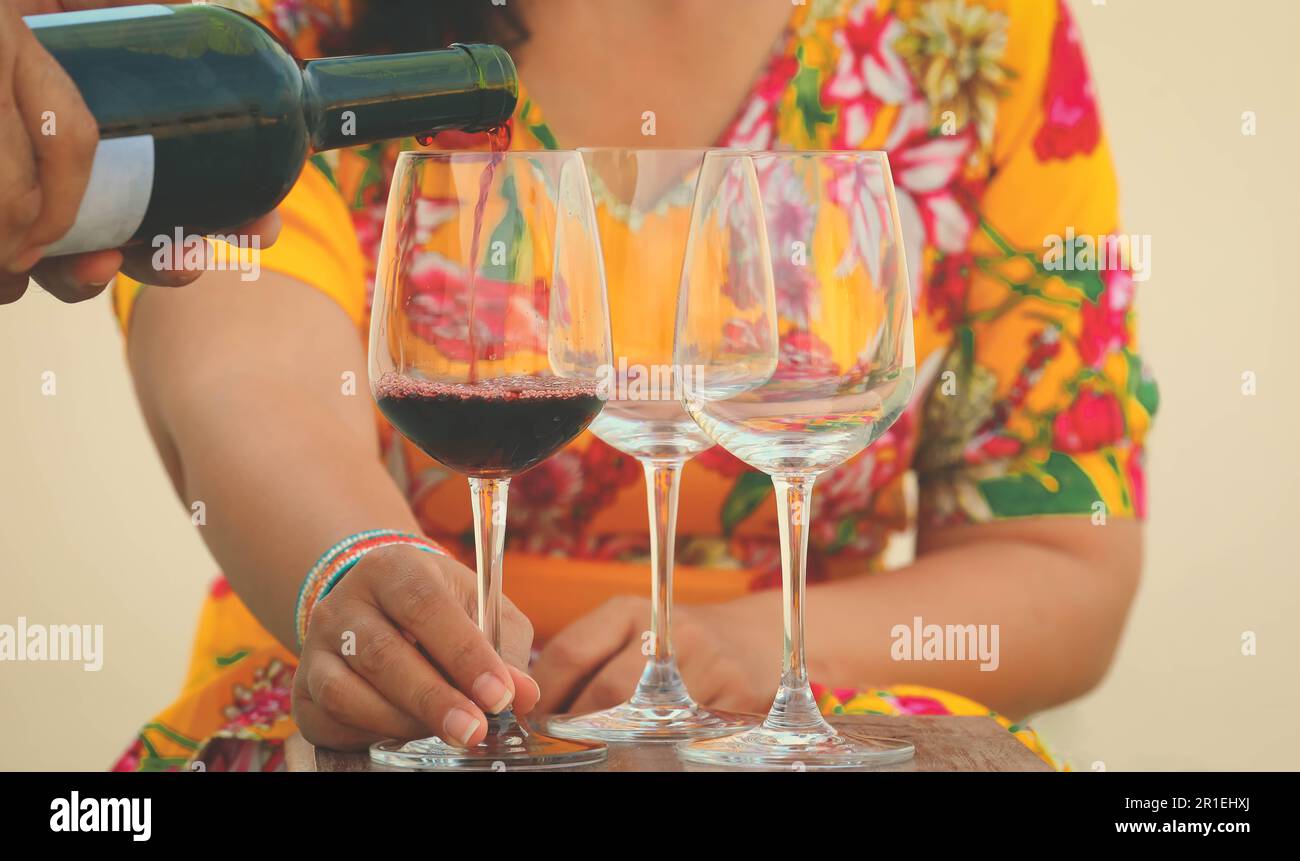 Hand poring red wine to wine glasses on table Stock Photo