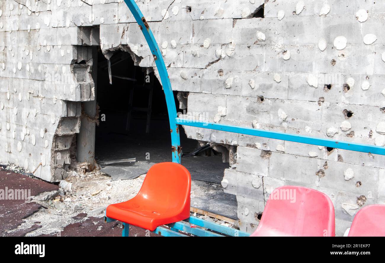 War in Ukraine. Broken plastic benches for fans on the podium, in a destroyed football stadium in a children's football school. The consequences of sh Stock Photo