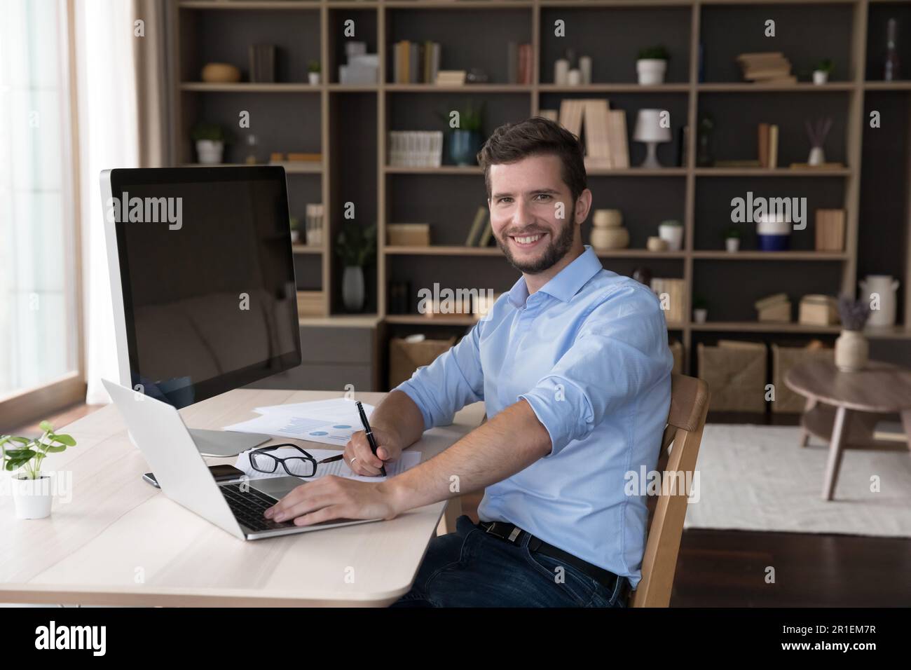 Happy freelance professional programmer sitting at table with workstation Stock Photo