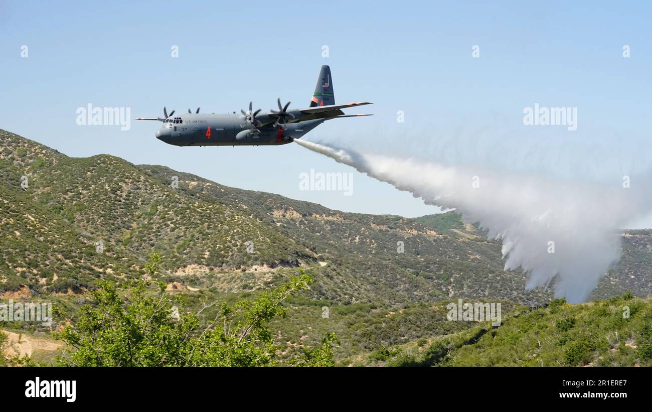 A U.S. Air National Guard MAFFS (Modular Airborne Fire Fighting System) equipped C-130J Super Hercules assigned to the 115th Airlift Squadron discharges a line of water simulating a fire retardant drop during aerial wildfire suppression training with the U.S. Forest Service and the California Department of Forestry and Fire Protection (CAL FIRE) in the mountains of the Angeles Forest above Santa Clarita, California, May 12, 2023. This week's training will culminate the second iteration of MAFFS training and celebrate a 50-year interagency partnership between the Department of Defense and the U Stock Photo