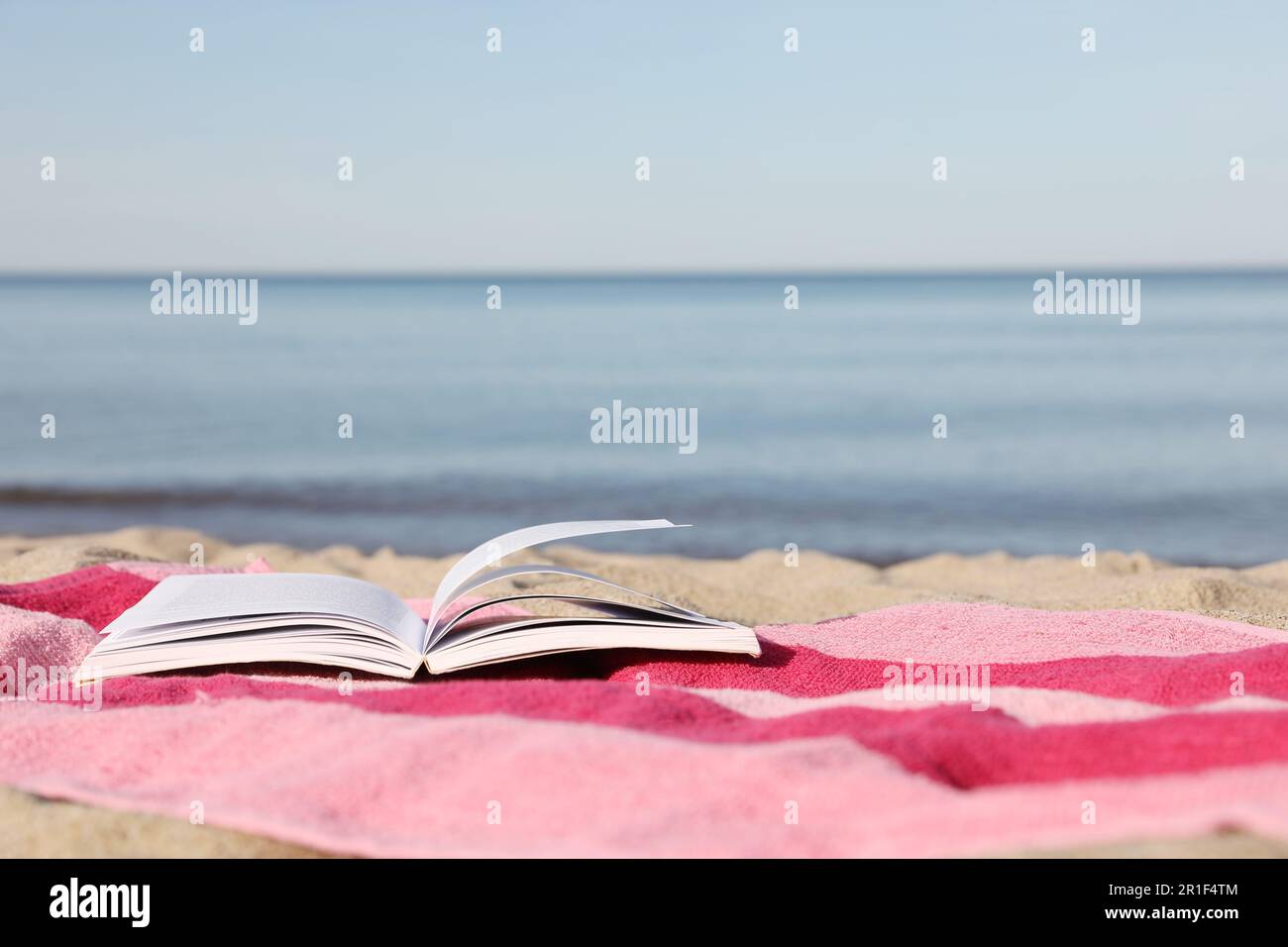 Beach towel and open book on sand near sea, space for text Stock Photo ...