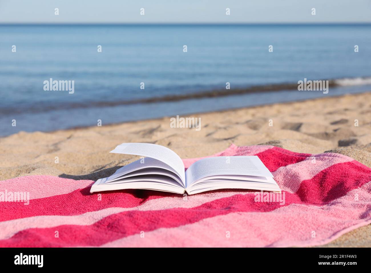 Beach towel and open book on sand near sea, space for text Stock Photo ...