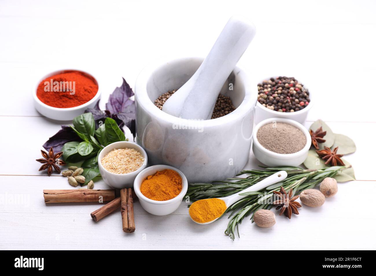 Mortar with pestle and different spices on white wooden table Stock Photo