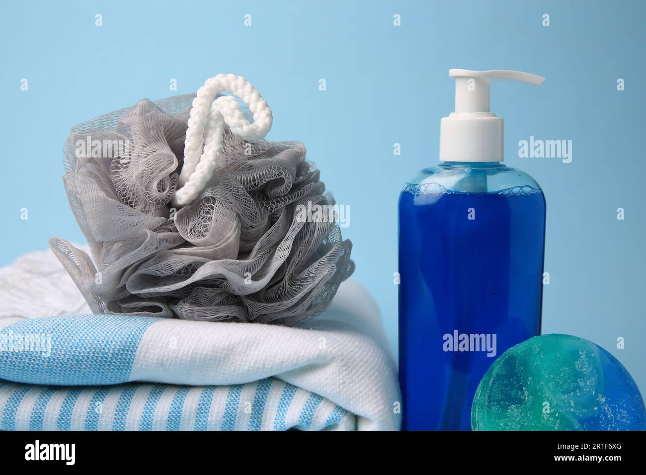 Grey shower puff, cosmetic products and towel on light blue background