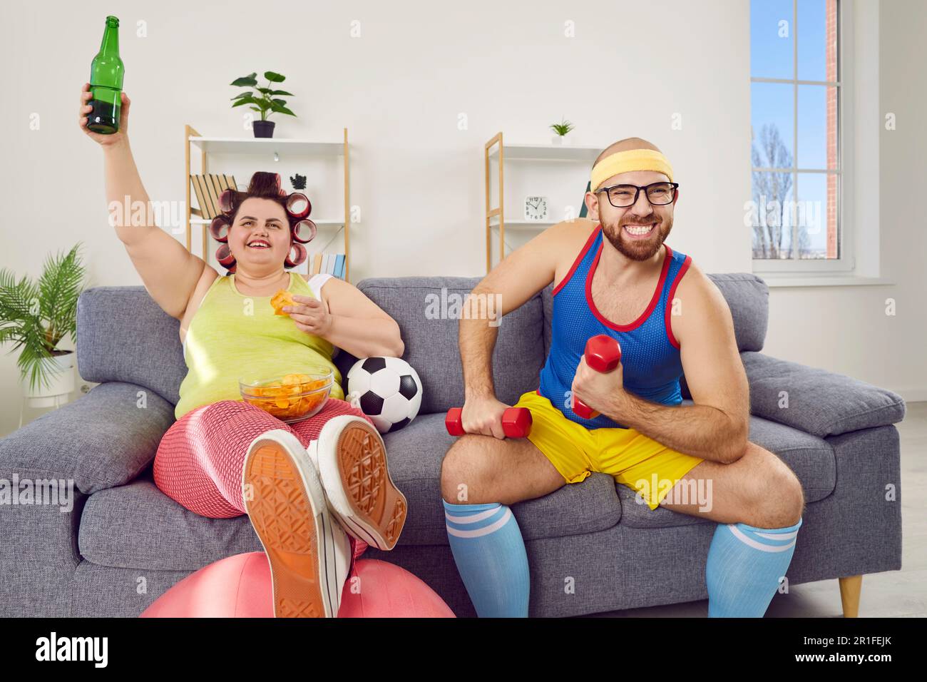 Fun young couple in sportswear watching football sports games sitting on sofa at home together. Stock Photo