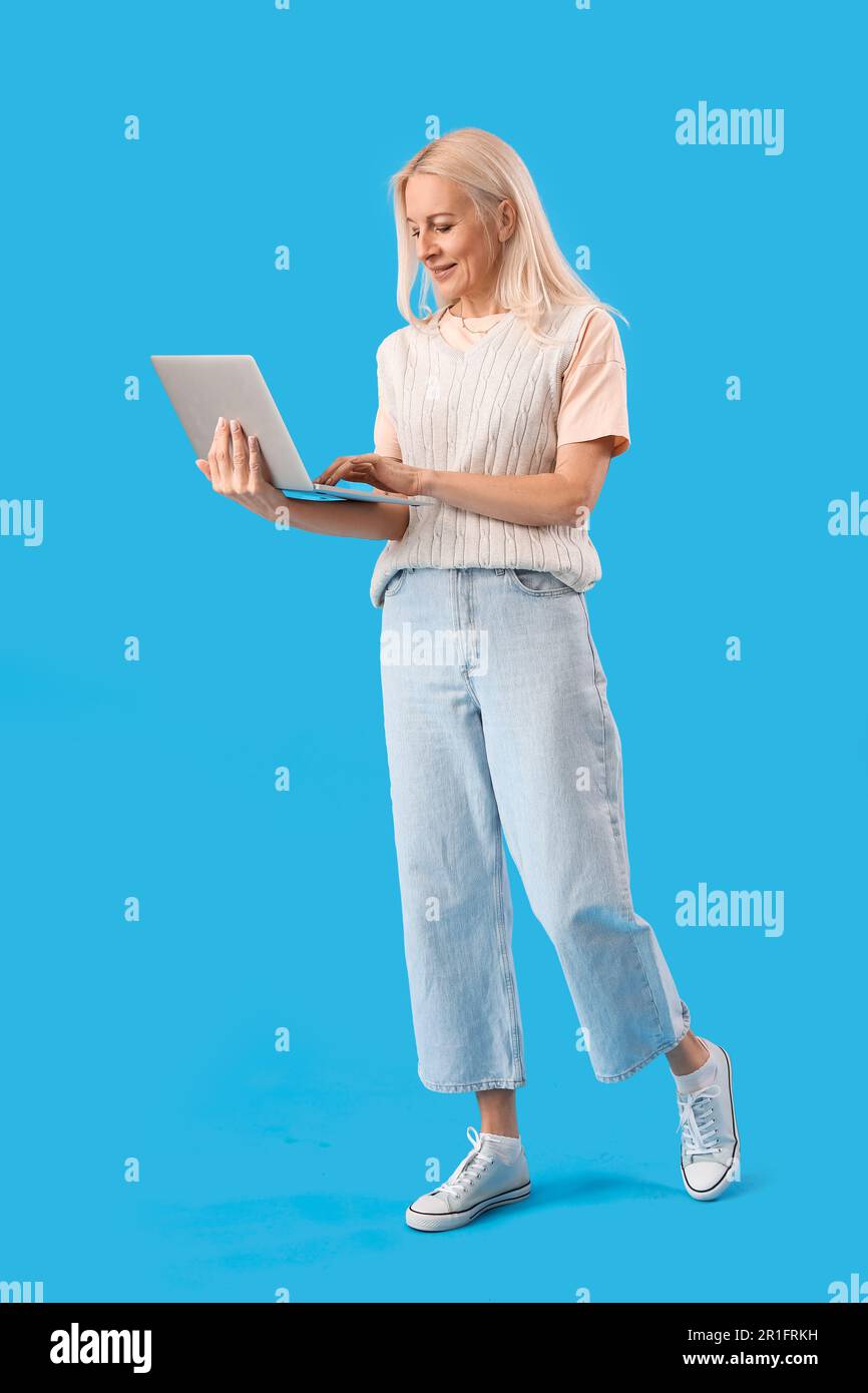 Mature female programmer working with laptop on blue background Stock ...