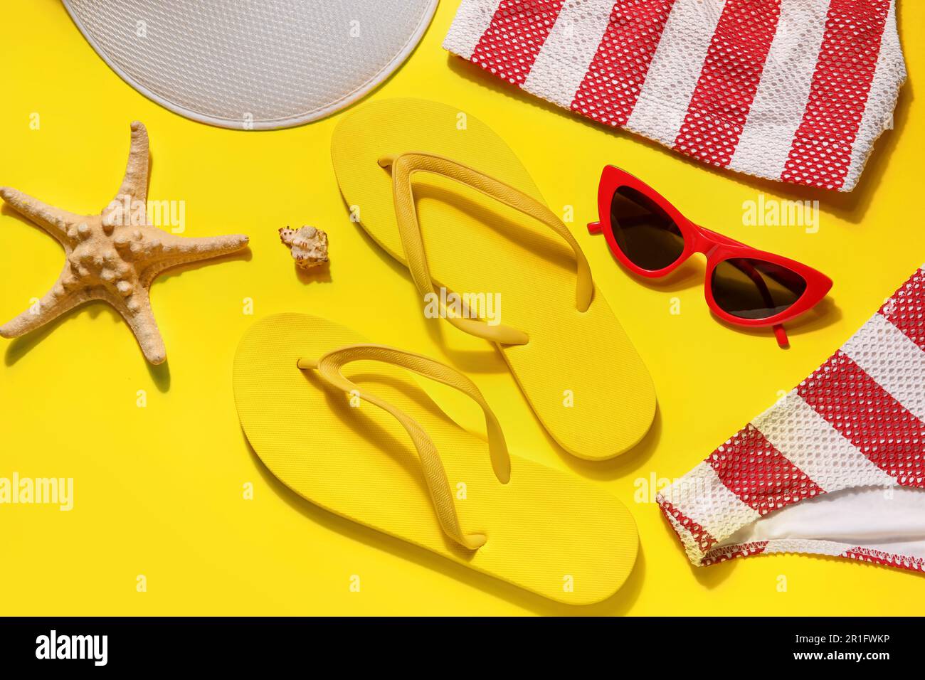 Flip flops with swimsuit, sunglasses and tennis hat on yellow ...