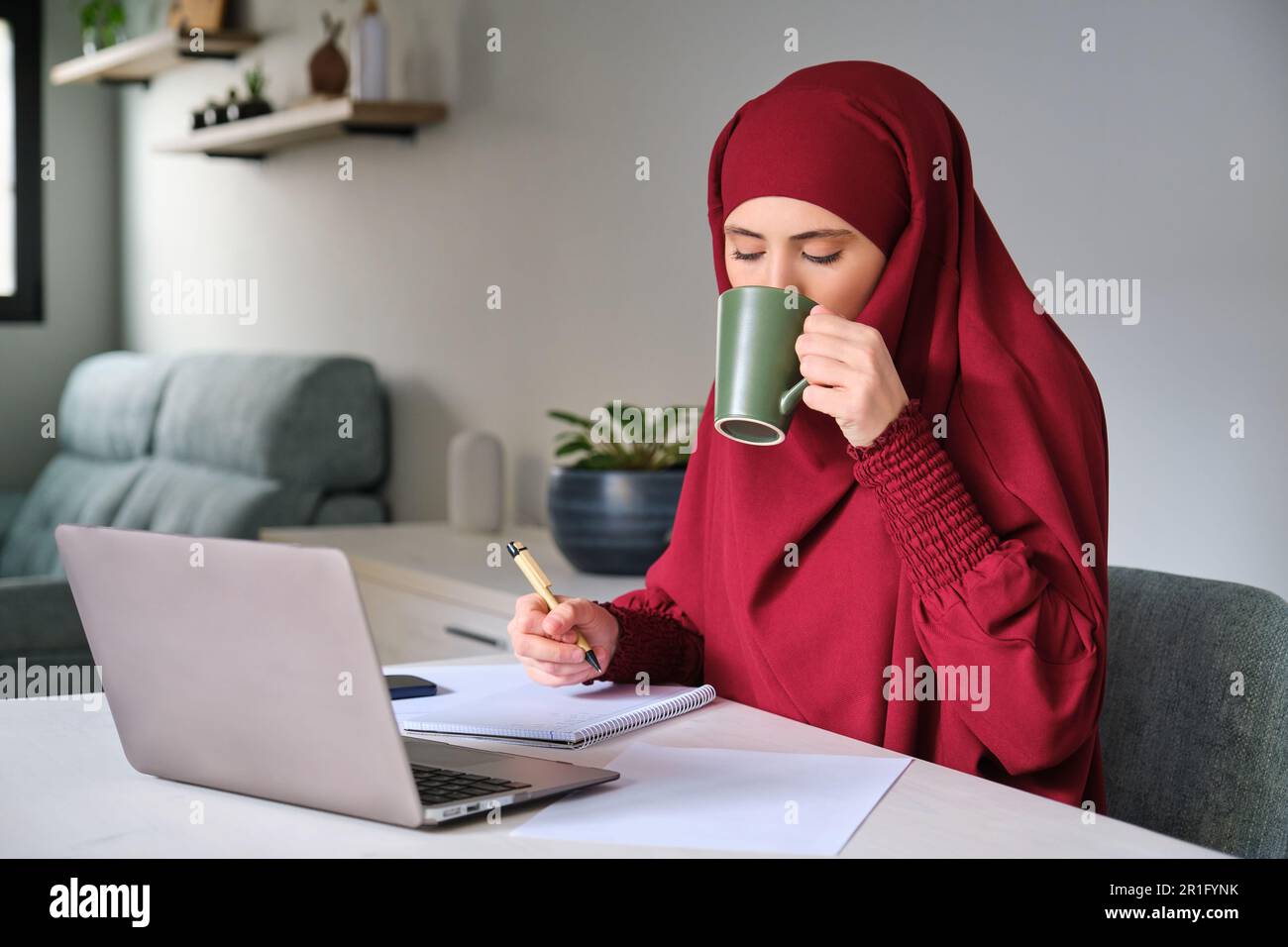 Muslim young woman in hijab drinking coffee while working at home Stock ...