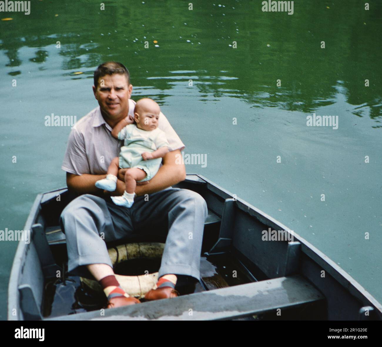 Man sitting in a rowboat, holding an infant ca. 1950s Stock Photo