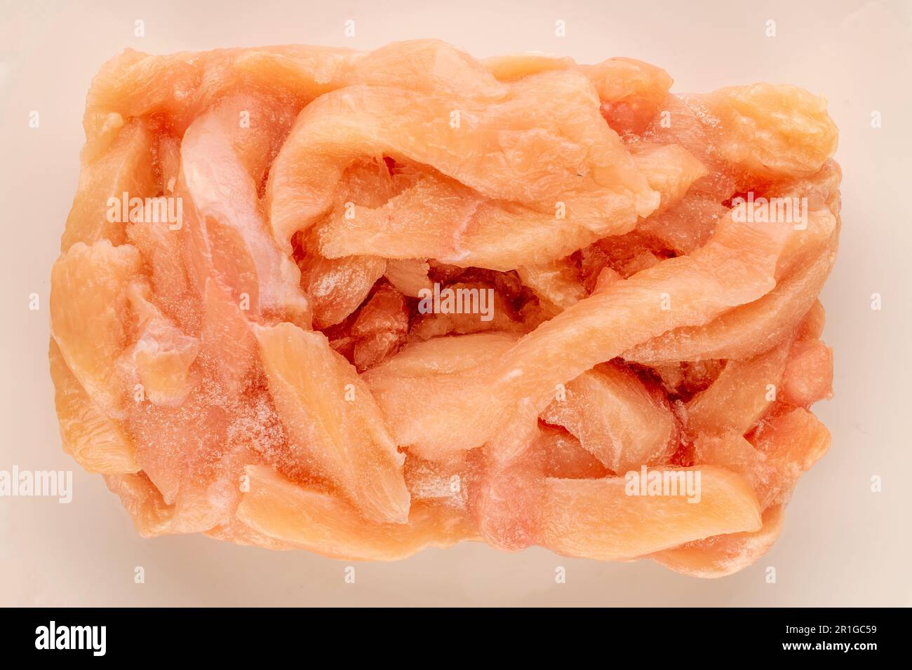Pieces of frozen chicken meat on a white porcelain plate, macro, top