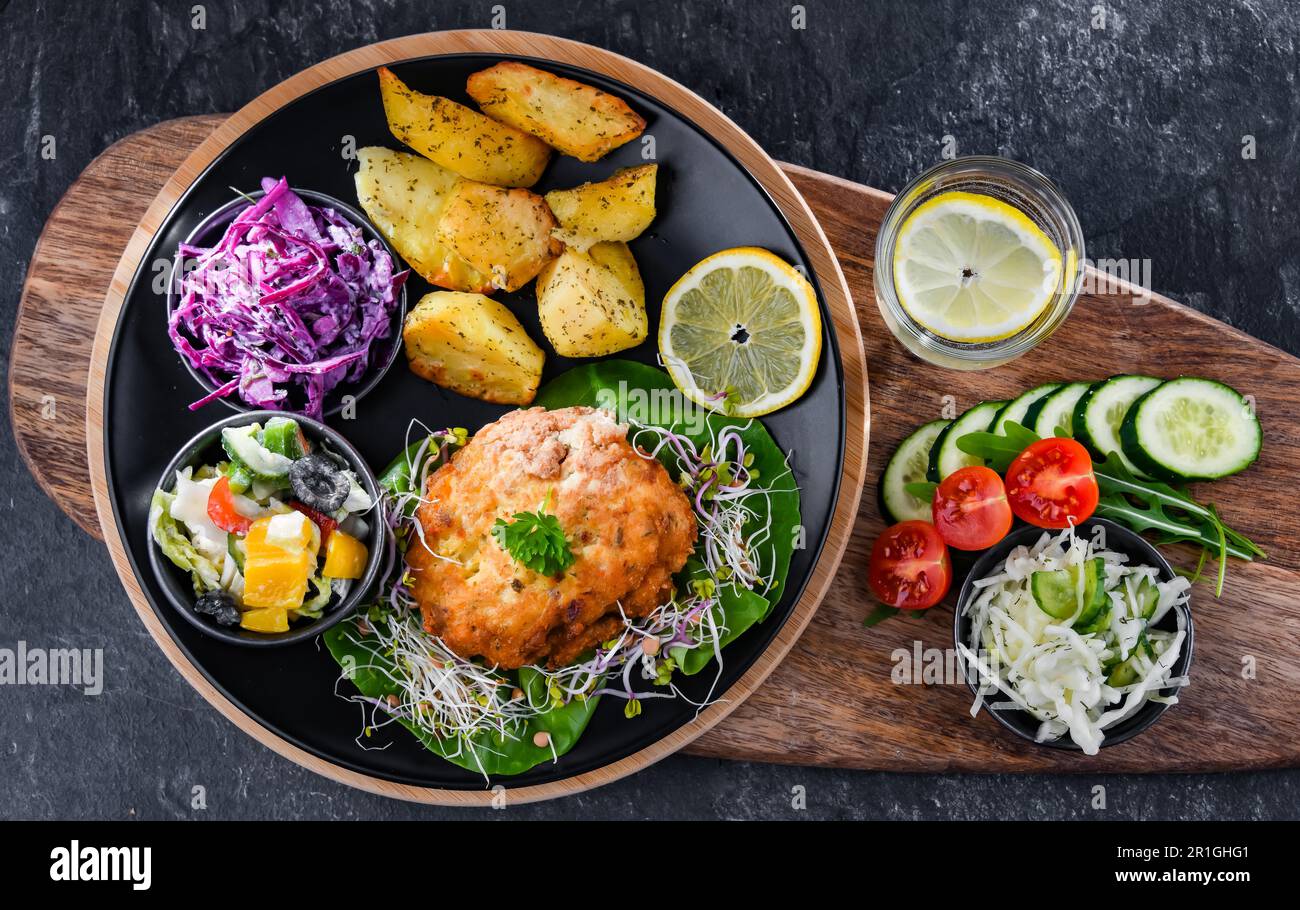 Pulled chicken cutlet coated with breadcrumbs with potatoes and vegetable salads Stock Photo